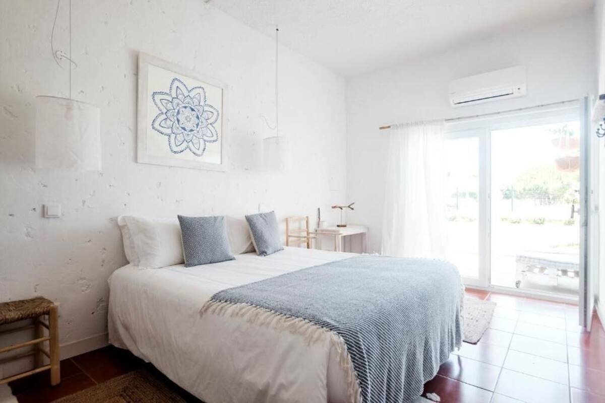 A bedroom with a large bed, a small table, and a chair. There is a window with a view of the outside.