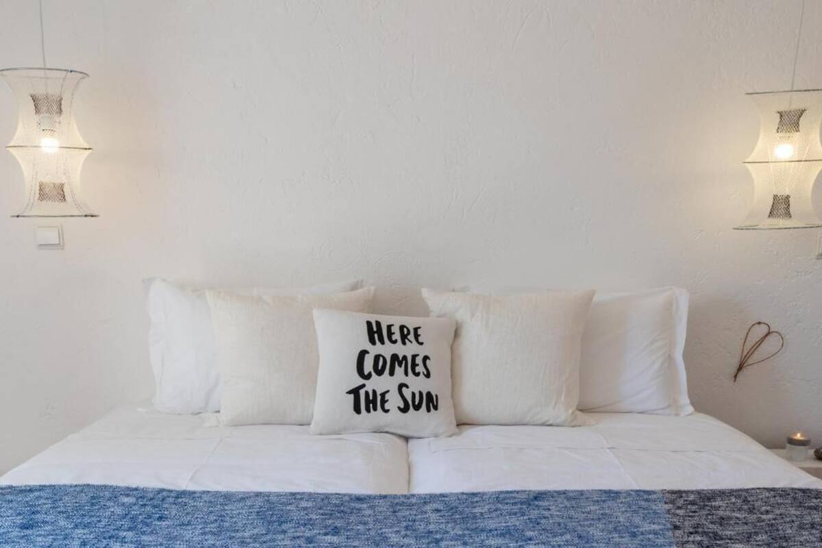 A bed with white bedding and a pillow with text, two wall-mounted lamps, and a small wall decoration.