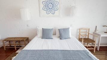 A bedroom with a bed, two pillows, a bedside table, a chair, a rug, and a wall art piece.