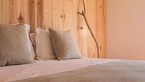 A bed with a white sheet and two beige pillows against a wooden wall. - Utopia (Aljezur)
