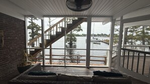 Ein Zimmer mit einem großen Fenster mit Blick auf ein Gewässer, einer Treppe, die nach draußen führt, und einem Korbsessel mit Kissen.