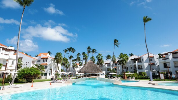 A resort with a swimming pool, palm trees, and white buildings with red roofs.
