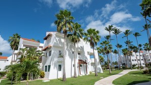 A white building with a red-tiled roof, surrounded by palm trees and a clear blue sky.