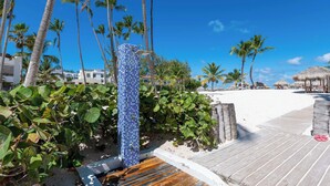 A wooden deck leading to a beach with palm trees and a blue-tiled structure.
