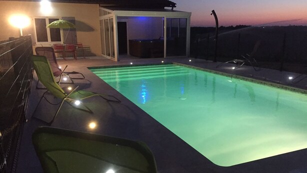A rectangular swimming pool with a glass bottom, surrounded by green chairs and a covered seating area.