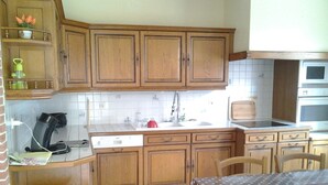 A kitchen with wooden cabinets, a white countertop, a sink, a stove, and a dining table with a polka dot tablecloth.