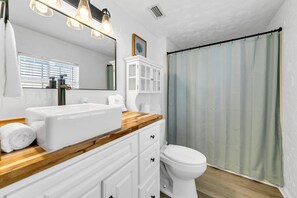 A bathroom with a white sink, wooden countertop, white cabinets, a white toilet, and a shower curtain. - Private Pool! Hot Tub! Golf Cart! Bikes! Walk to Beach! Paddle Boards! (Panama City Beach)