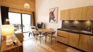 A modern kitchen with wooden cabinets and a black countertop, a dining area with a round table and chairs, and a large window with curtains.