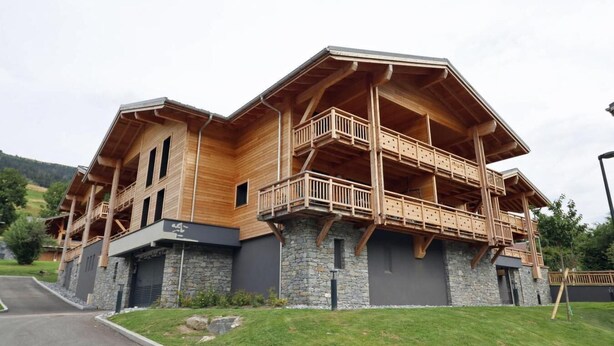 A multi-story wooden house with balconies, stone foundation, and a driveway.