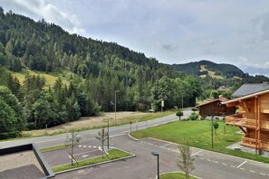 Um hotel com fachada de madeira, estacionamento e vista para uma montanha arborizada.