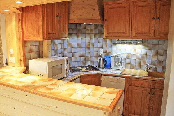 A compact kitchen with wooden cabinets, a microwave, a coffee maker, and a dishwasher.