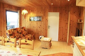 Interior acogedor de una cabaña de madera con un sofá, sillones, una mesita y un cuadro en la pared.
