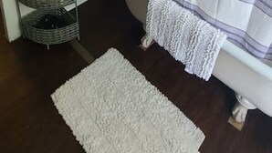 A bathroom with a white bathtub, a striped shower curtain, a white rug, and a wicker basket with towels.