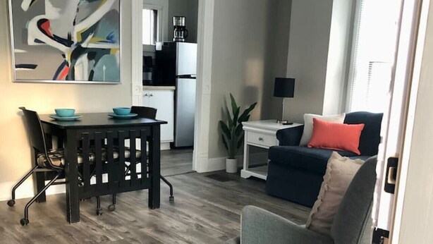 Een moderne woonkamer met een eethoek, een keuken op de achtergrond, en een groot abstract schilderij aan de muur.