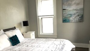 Een slaapkamer met een groot bed, een nachtkastje, een raam met zonwering en een schilderij aan de muur.