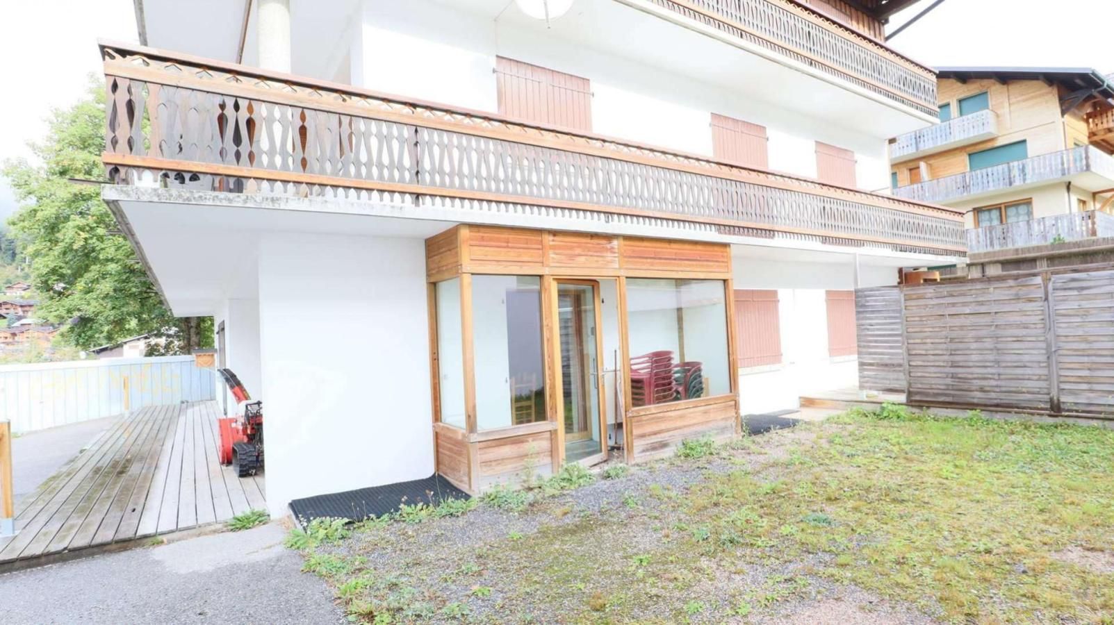 Un bâtiment à deux étages doté d’un balcon en bois, d’une entrée avec une porte vitrée et d’un petit jardin.