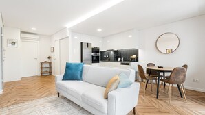En moderne stue med en sofa, et spisebord med stole, et køkken og et stort spejl på væggen.