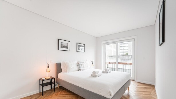 Et moderne soveværelse med en stor seng, et natbord med lampe, og udsigt til det fri gennem et stort vindue.