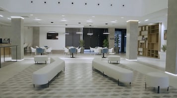 Un vestíbulo moderno con sofás blancos, un mostrador de recepción y una planta grande.