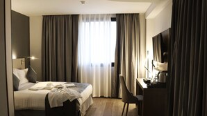 A hotel room with a bed, a desk, a chair, a television, and curtains. - Bayazid Hotel (Setif)