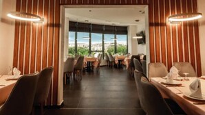 A restaurant with a modern interior, featuring wooden paneling and a view of a cityscape through large windows. - Bayazid Hotel (Setif)
