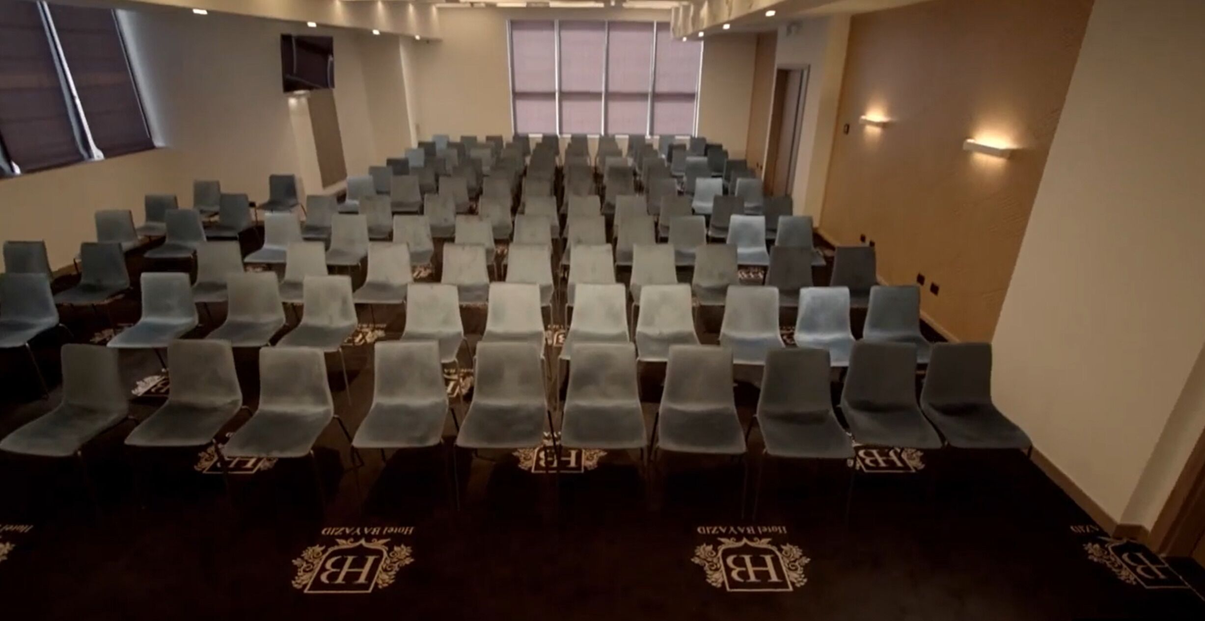 Un salón de conferencias con filas de sillas grises y una alfombra con un logotipo.