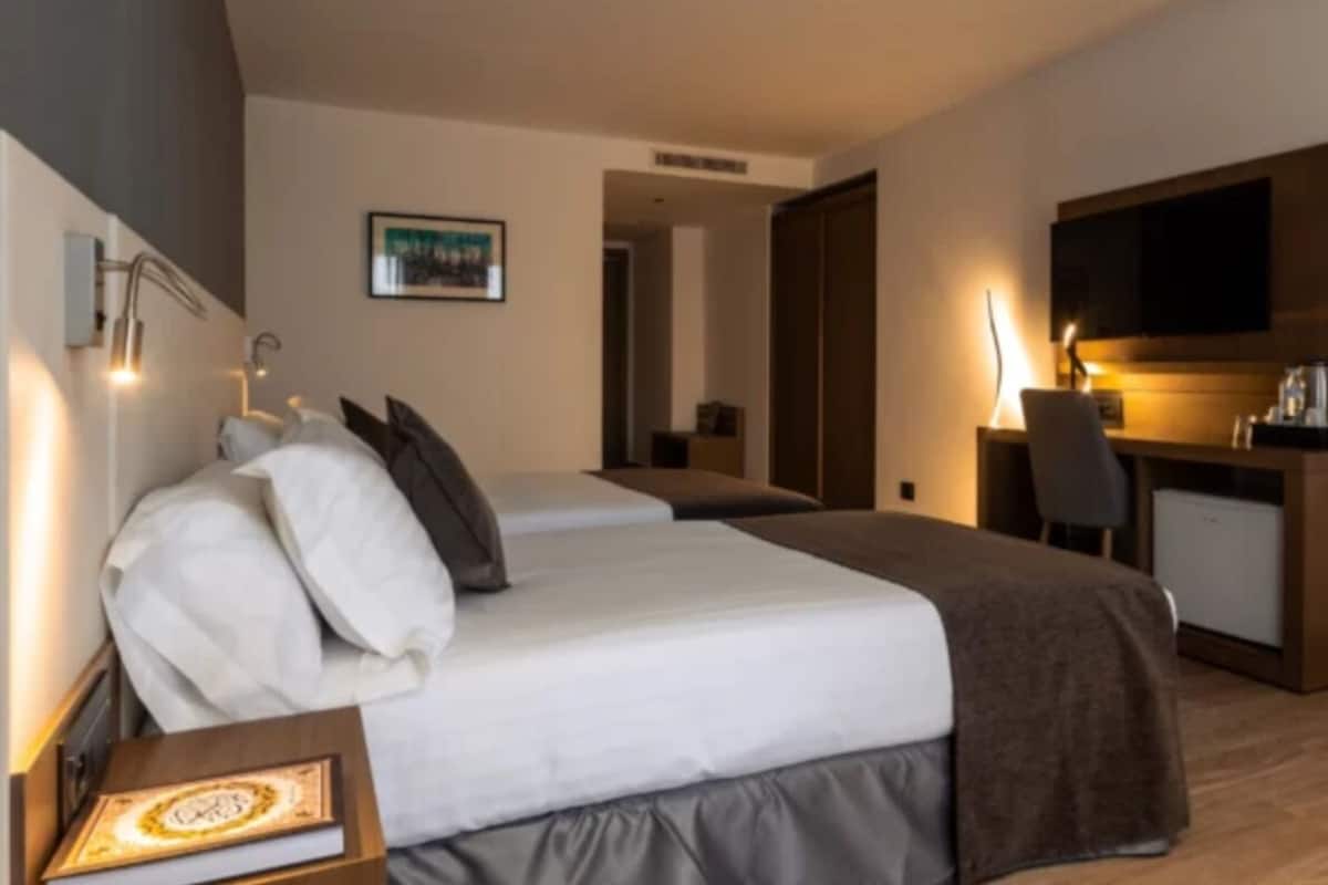 A hotel room with two beds, a desk, a chair, and a TV.