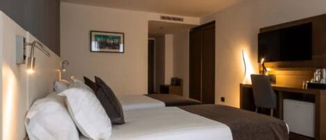 Habitación de hotel con dos camas, un escritorio, una silla y un televisor.