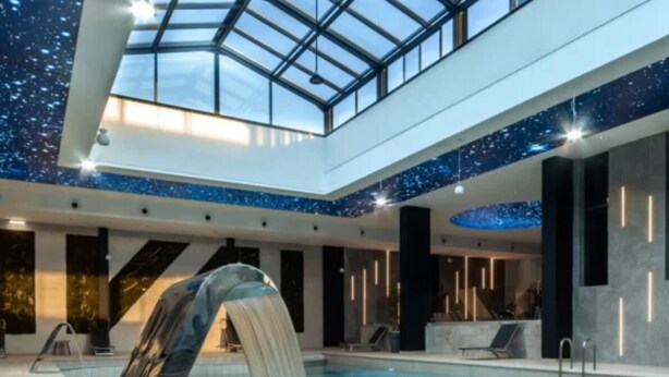 A modern indoor swimming pool with a waterfall feature, a glass ceiling, and a starry ceiling design. - Bayazid Hotel (Setif)
