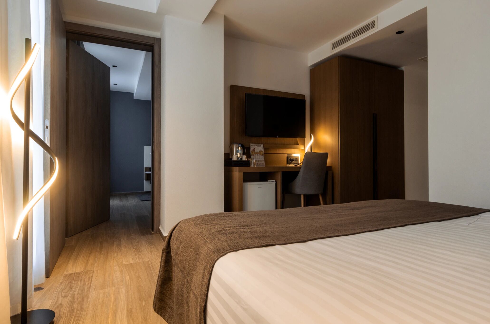 Habitación de hotel con cama, escritorio y silla, televisión y kitchenette.