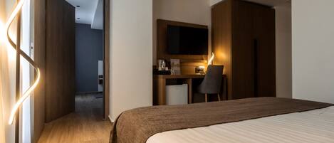 A hotel room with a bed, a desk with a chair, a television, and a kitchenette.