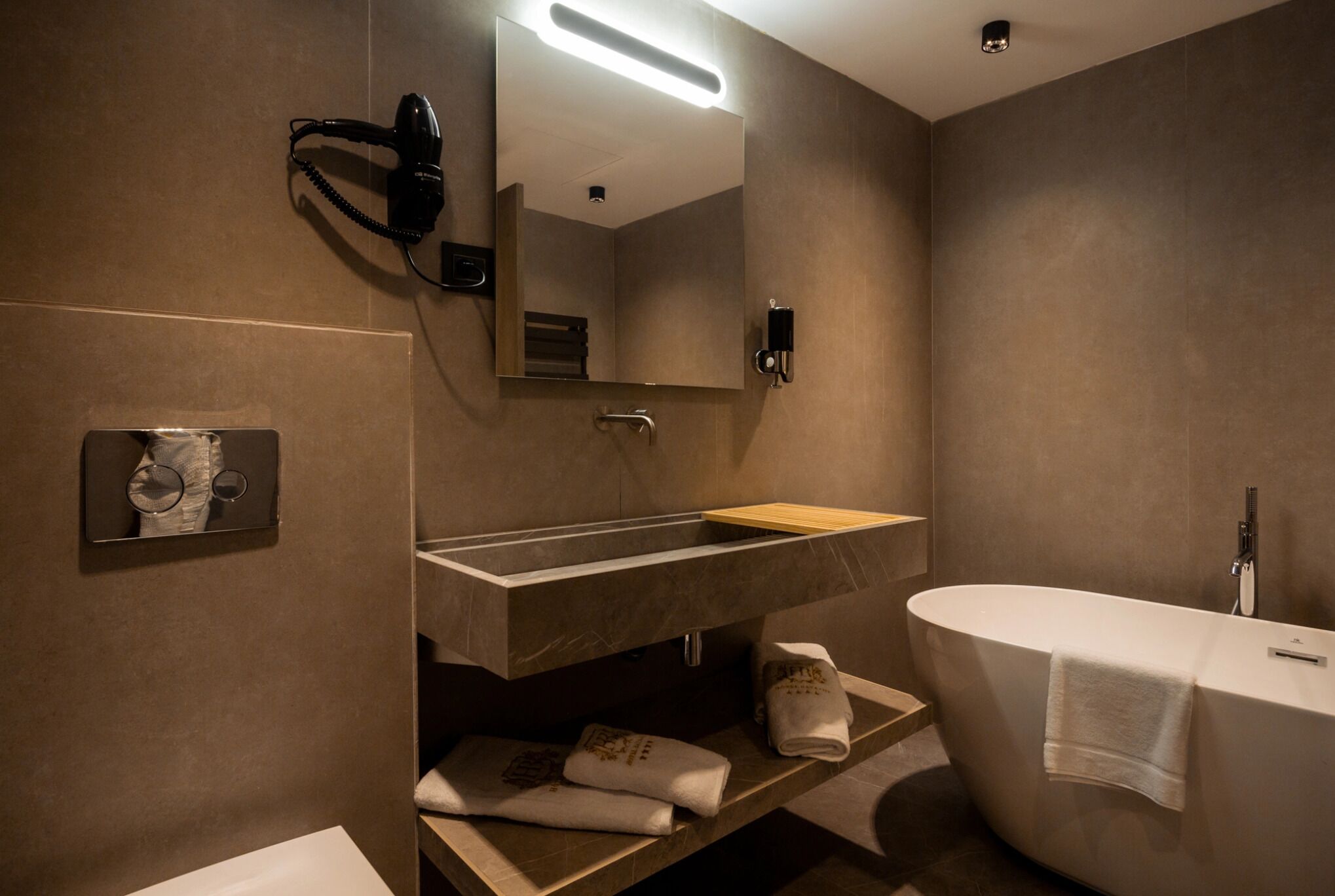A modern bathroom with a freestanding bathtub, a vanity with a mirror, and a hairdryer mounted on the wall.
