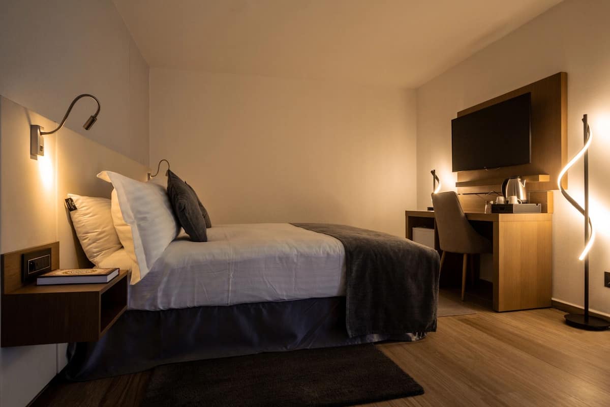 A modern bedroom with a bed, bedside table, lamp, desk, chair, and a TV.