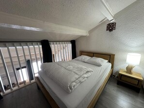 A bedroom with a bed, a nightstand with a lamp, and a window with blinds.