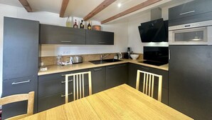 Une cuisine de taille réduite, dotée de meubles de rangement sombres, d’une table à manger en bois et d’appareils électroménagers de base.
