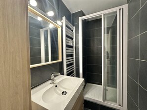 A modern bathroom with a large mirror, a white sink, and a glass shower enclosure.