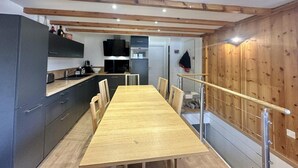 Une cuisine moderne avec des meubles de couleur sombre, une table à manger en bois et un escalier doté d’une rampe en bois.