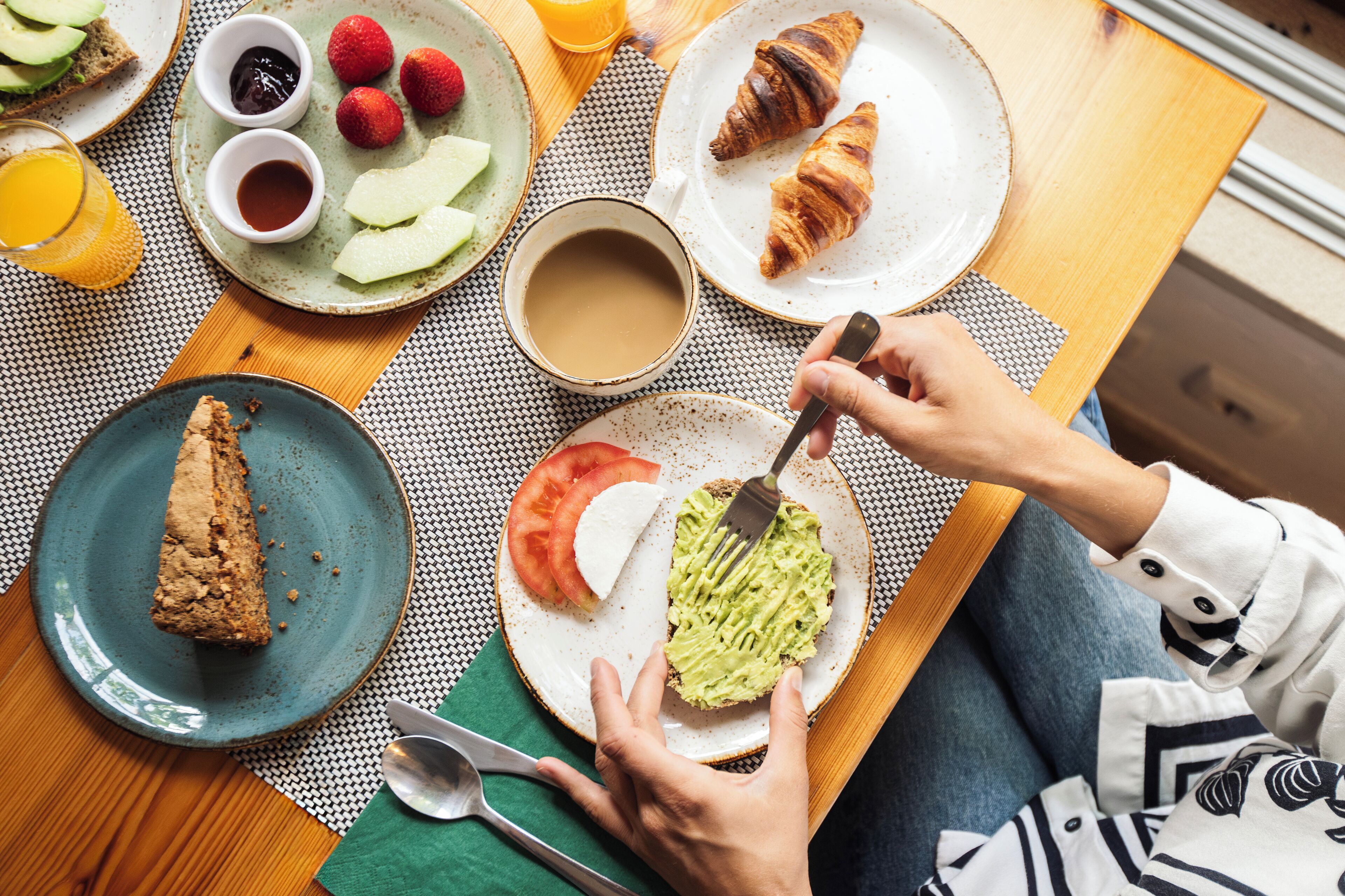 Un desayuno con croissants, tostadas, fruta y una taza de café sobre una mesa.