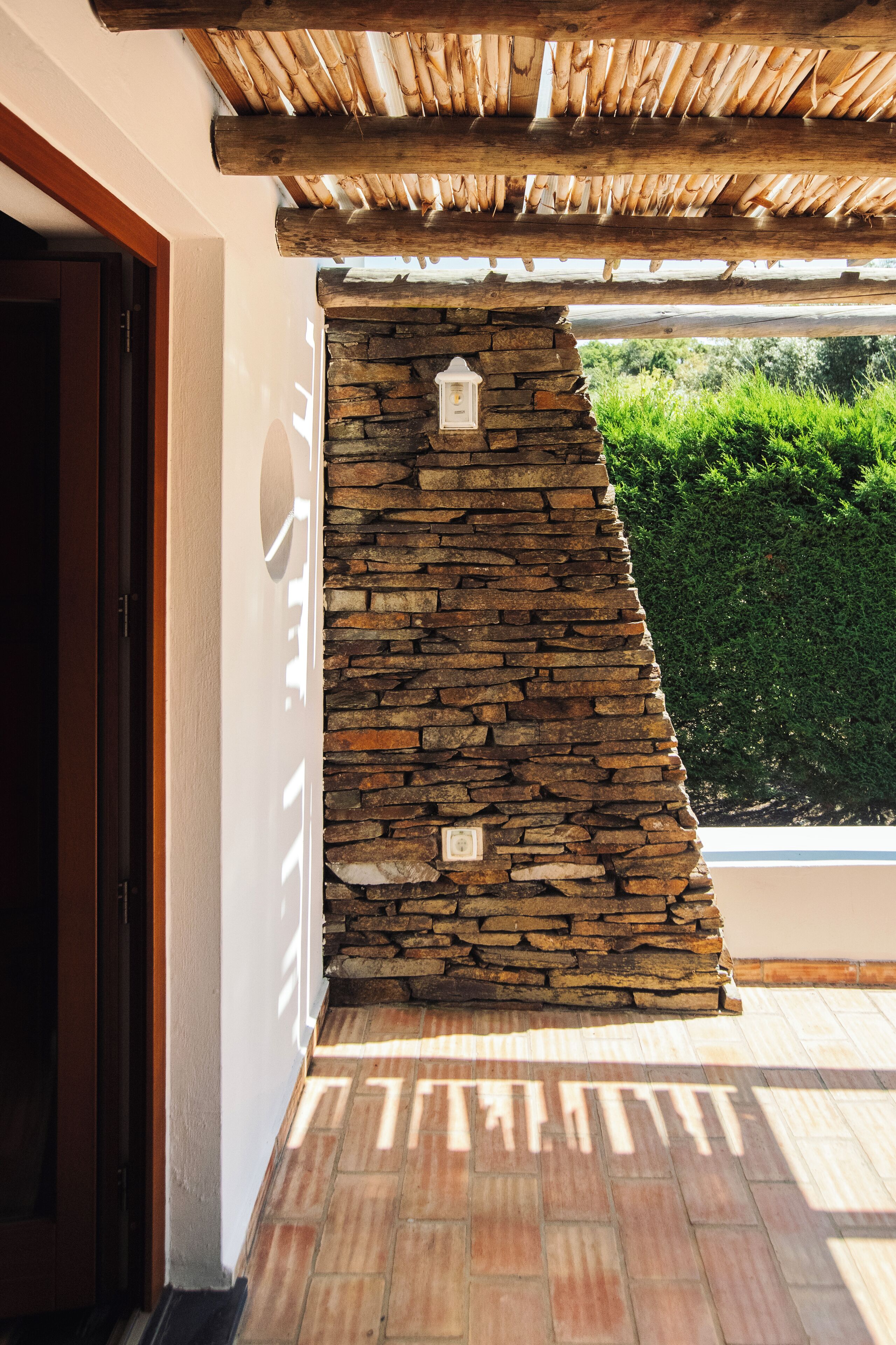 Un mur en pierre avec une lanterne, un plafond en bois et un sol carrelé.