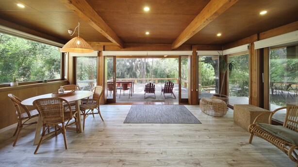 A spacious wooden interior with a dining area, wicker furniture, and large windows offering a view of the outdoors. - Monte da Vilarinha (Aljezur)