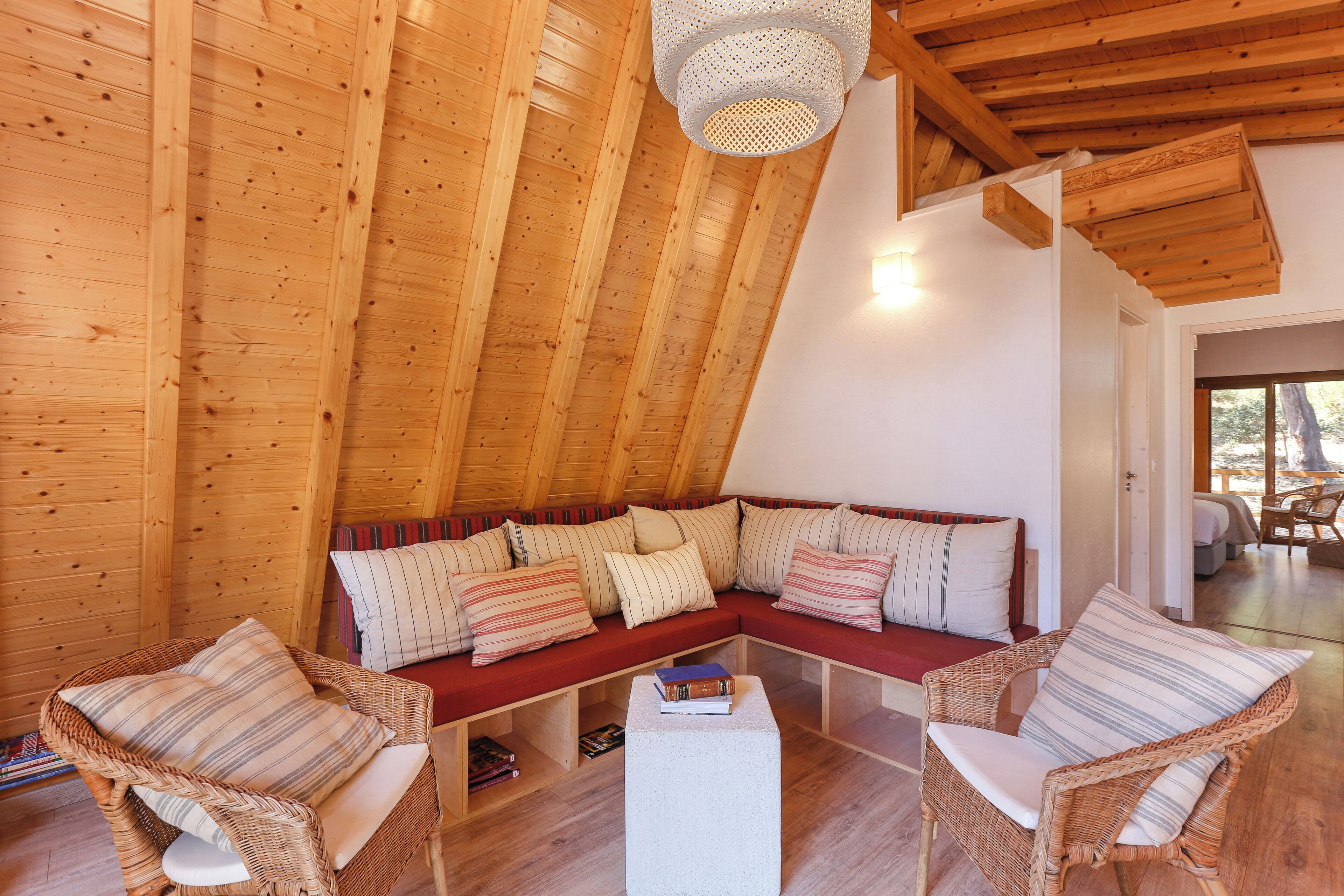 A cozy, wooden-floored room with a sloped ceiling, a sectional sofa with striped cushions, and wicker chairs.
