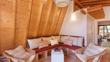 A cozy, wooden-floored room with a sloped ceiling, a sectional sofa with striped cushions, and wicker chairs.
