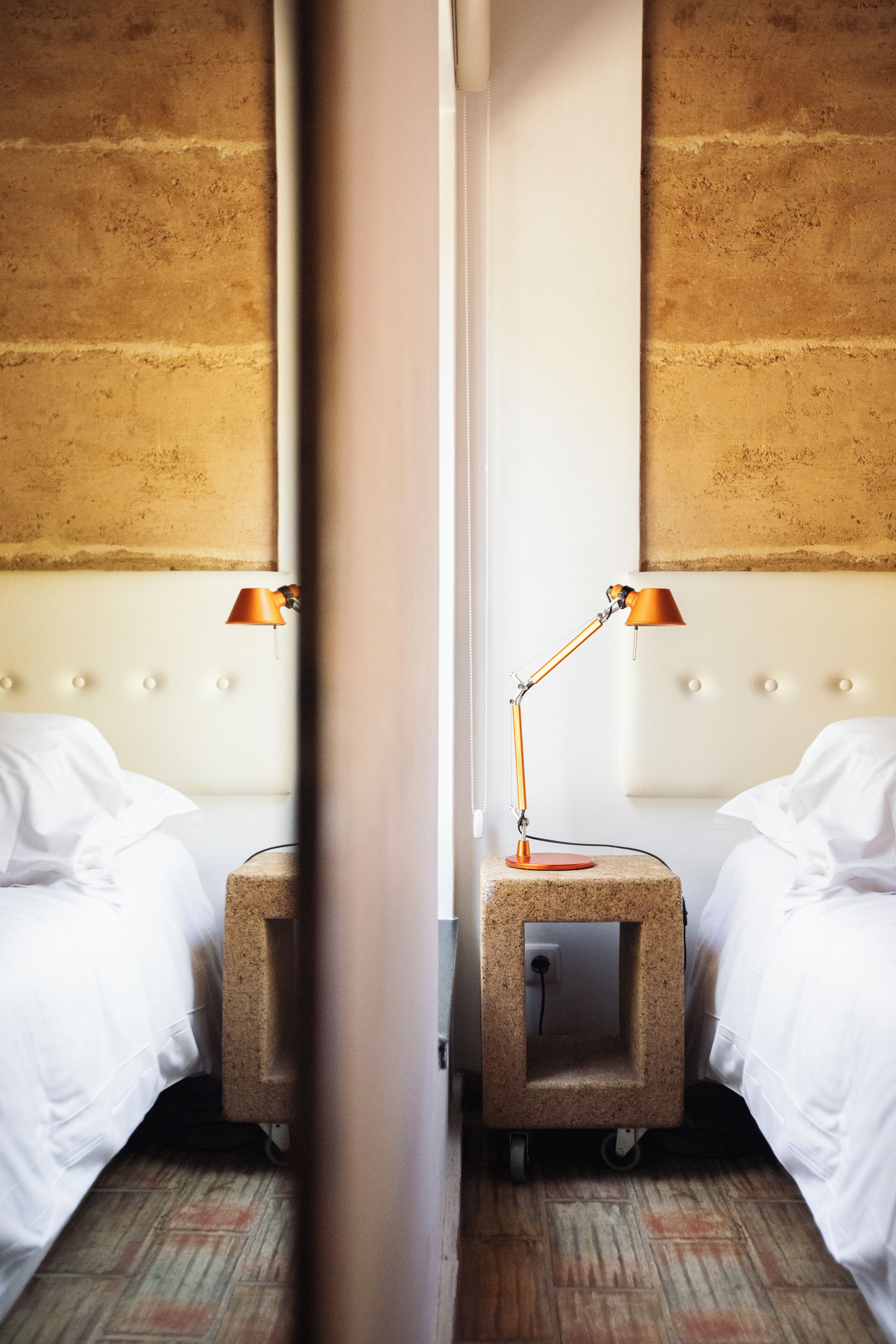 Ein Hotelzimmer mit zwei Betten, einem Nachttisch mit Lampe und einer Wand mit Backsteinmuster.