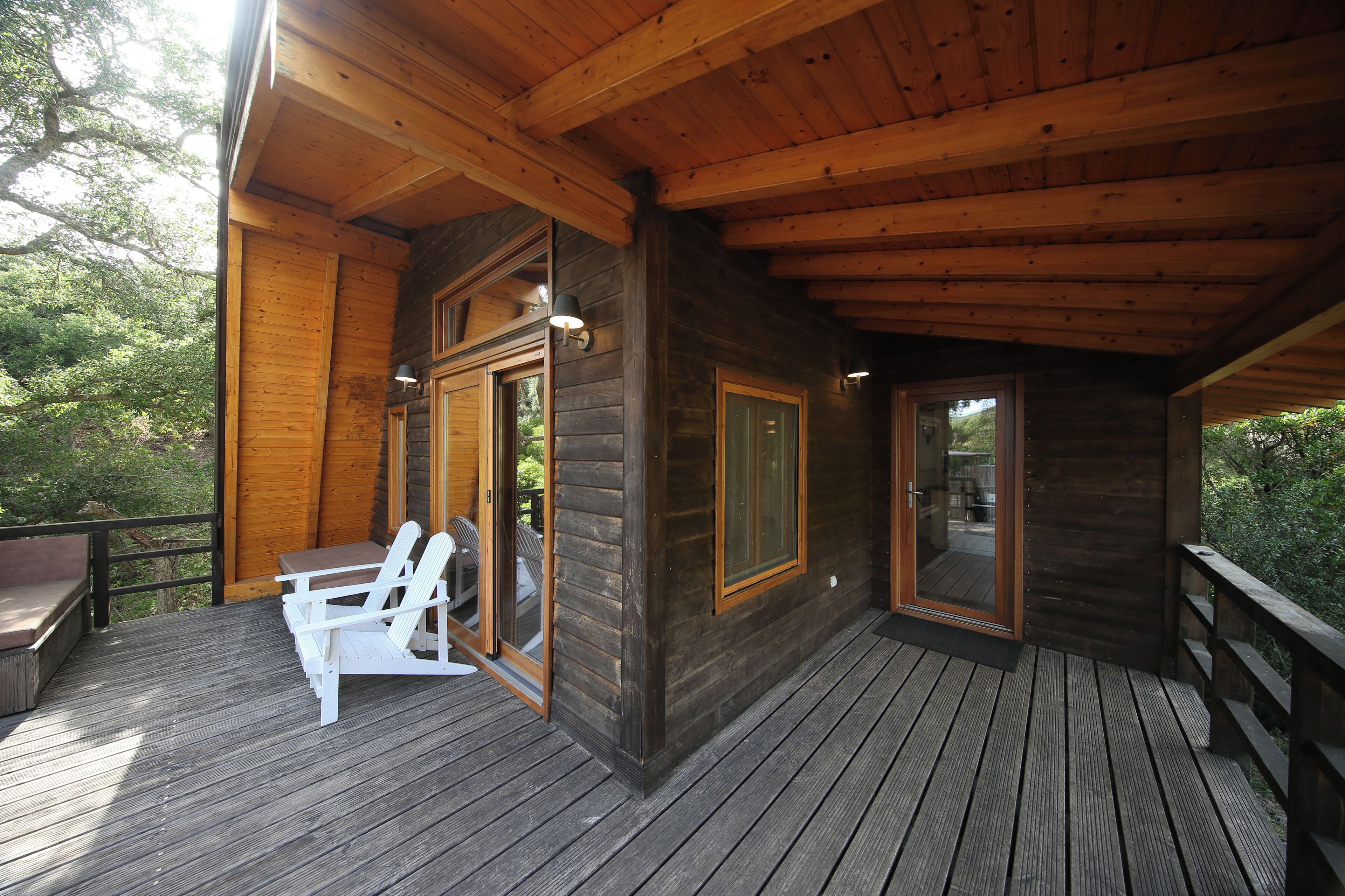 A wooden deck with a table and chairs, a glass door leading to a deck area, and a view of trees.