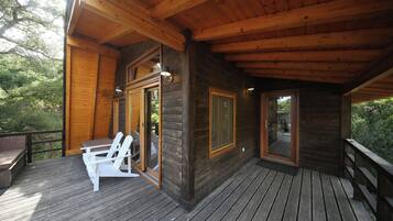 A wooden deck with a table and chairs, a glass door leading to a deck area, and a view of trees.