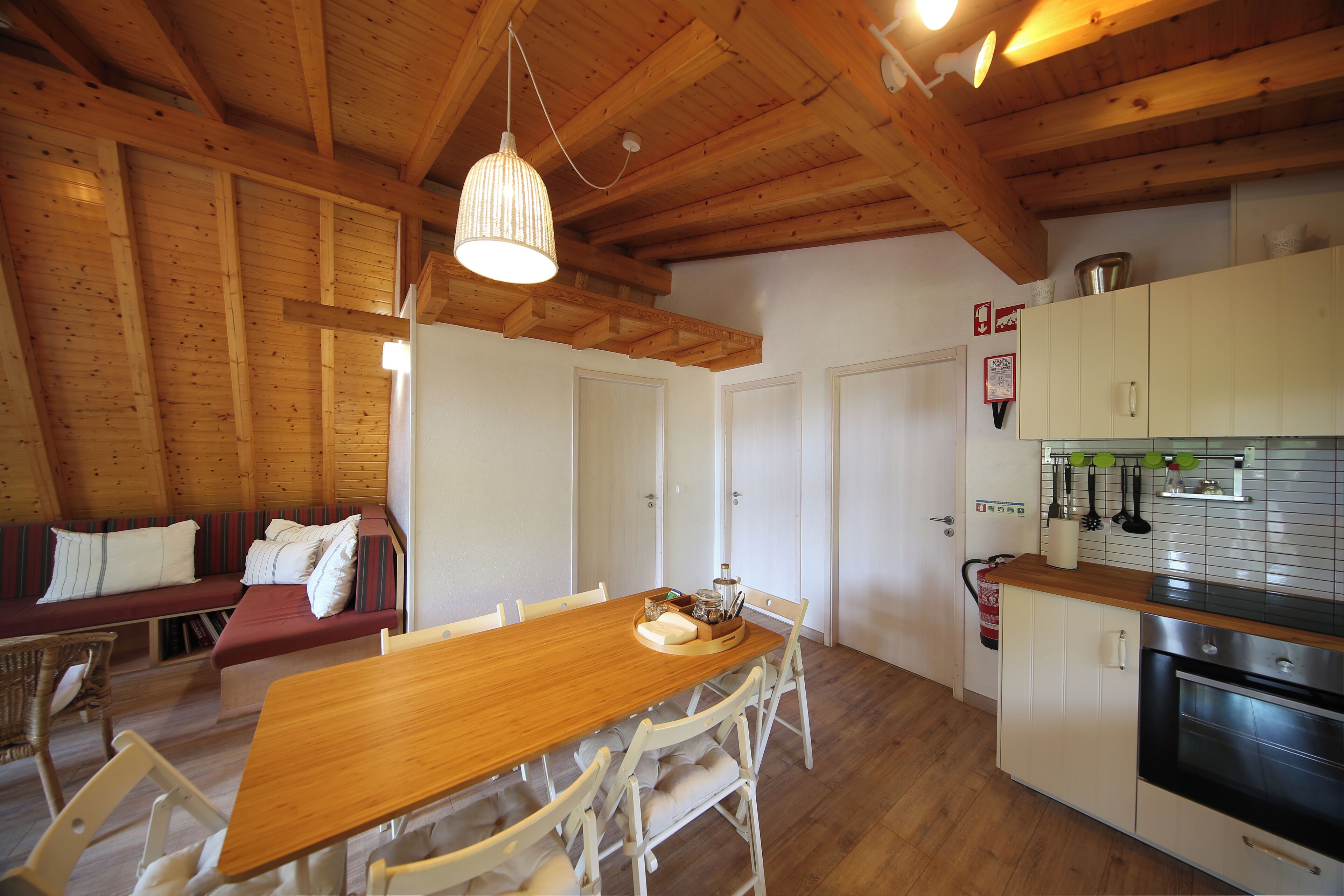 Una mesa de comedor de madera con sillas, techo de madera y una zona de cocina con armarios y estufa.