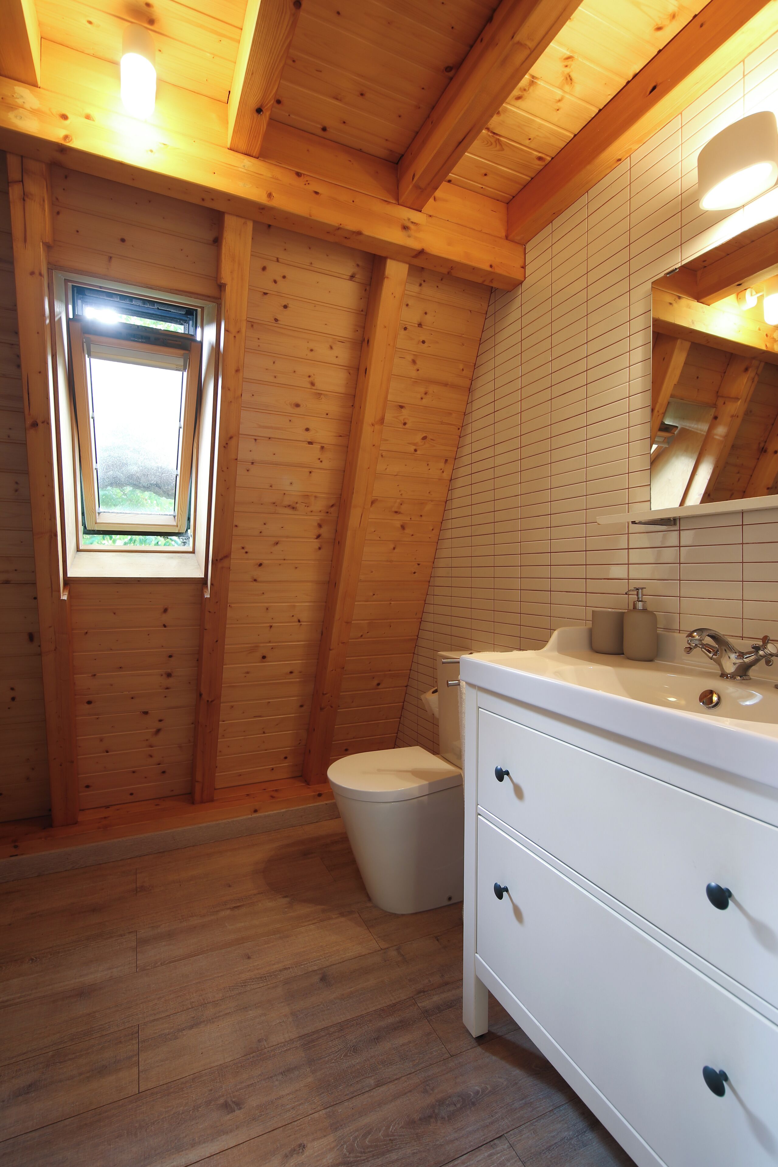 A wooden-paneled bathroom with a window, a toilet, and a white vanity with drawers.