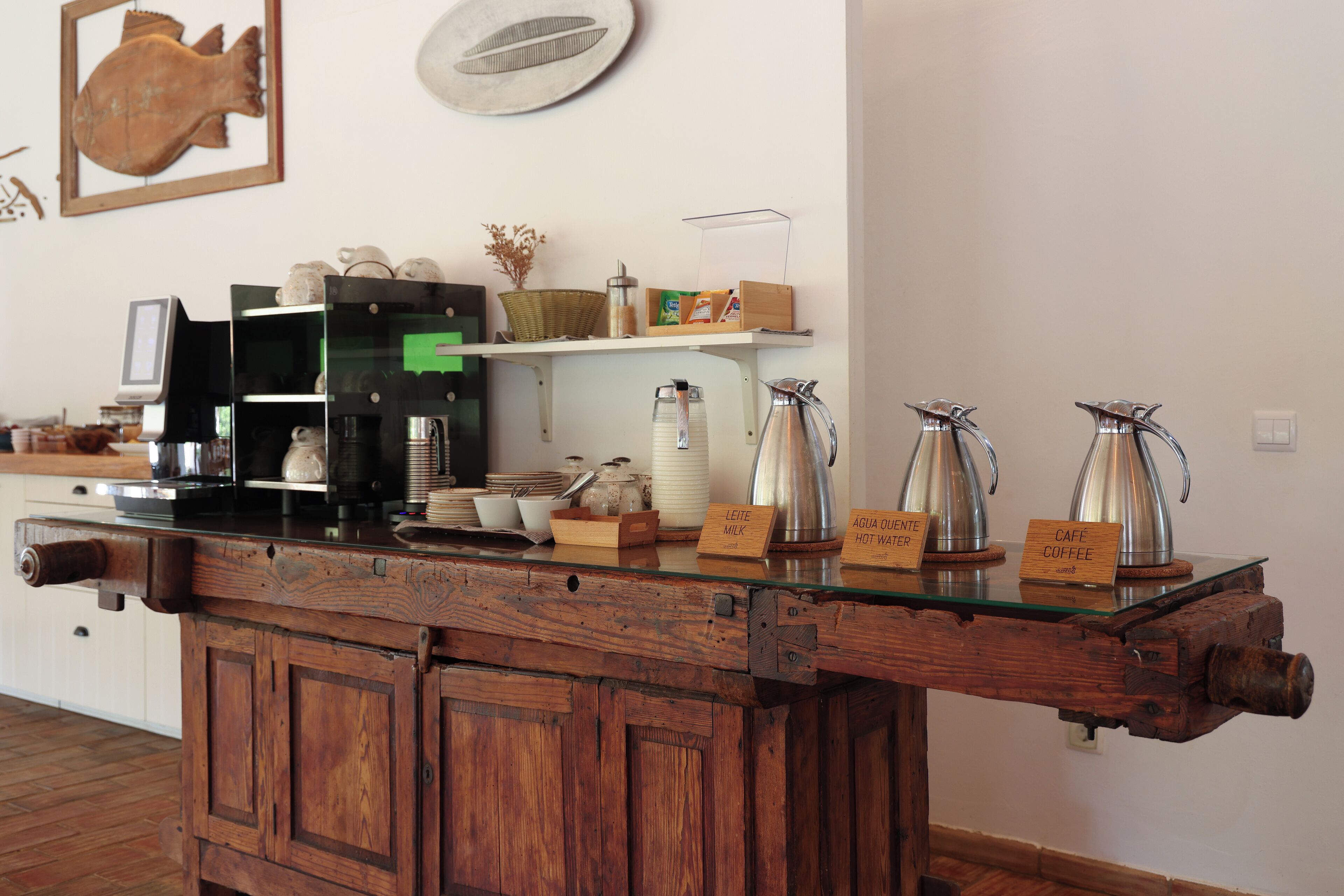 Ein rustikales Café mit einer Holztresen, einer Kaffeemaschine und verschiedenen Kaffeekannen, beschriftet mit Getränkebezeichnungen.