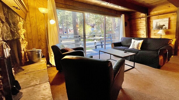 Interior acogedor de una cabaña con chimenea, un sofá, una mesa de centro y un ventanal con vistas al exterior.