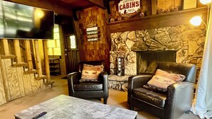 Interior acogedor de una cabaña con chimenea de piedra, dos sillones de cuero, una mesa de centro y un letrero que dice "Lakeside Cabins".